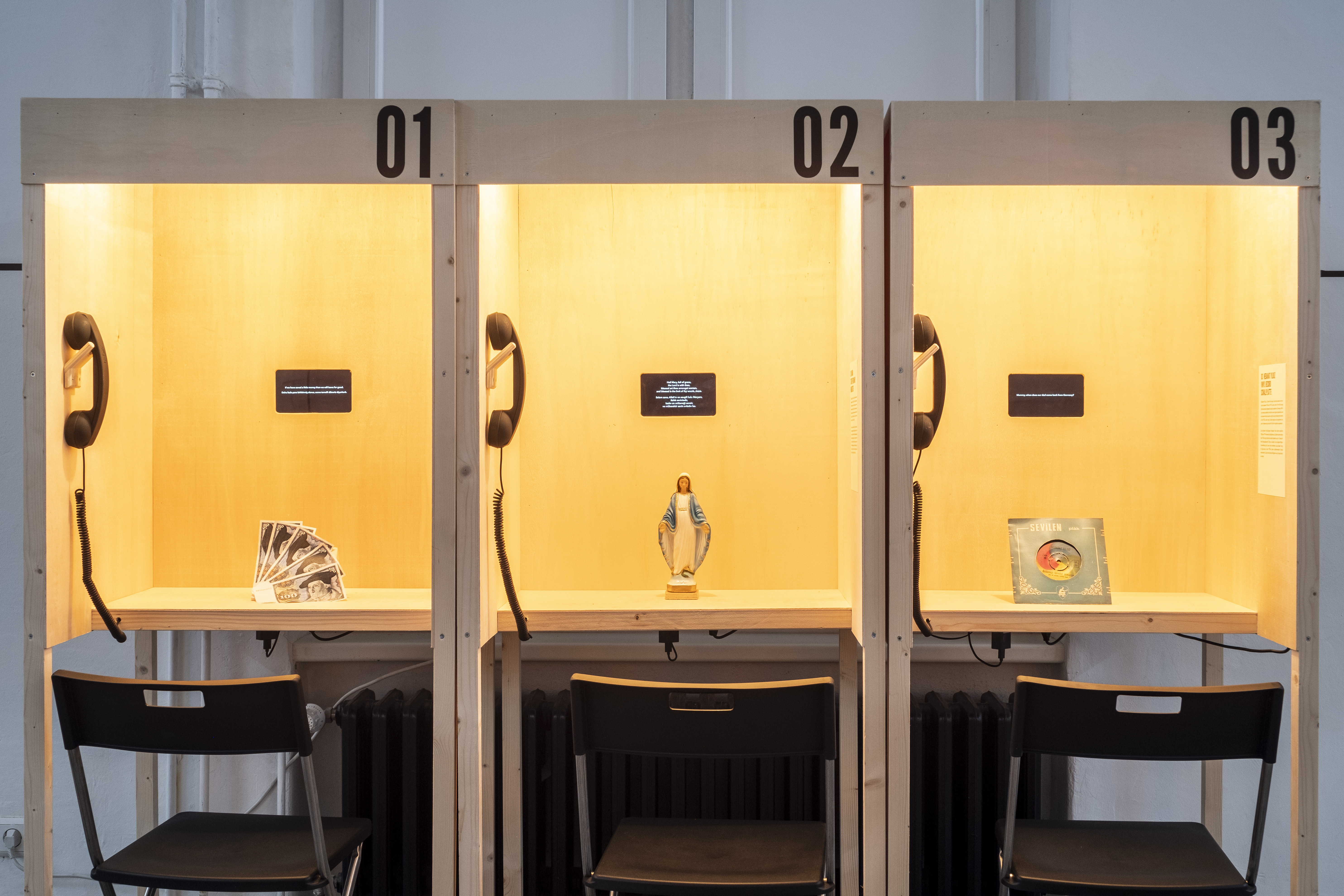 In drei offene Telefonkabinen sind jeweils alte 100-D-Mark-Scheine, eine Marienstatue und eine Schalplatte zu sehen.