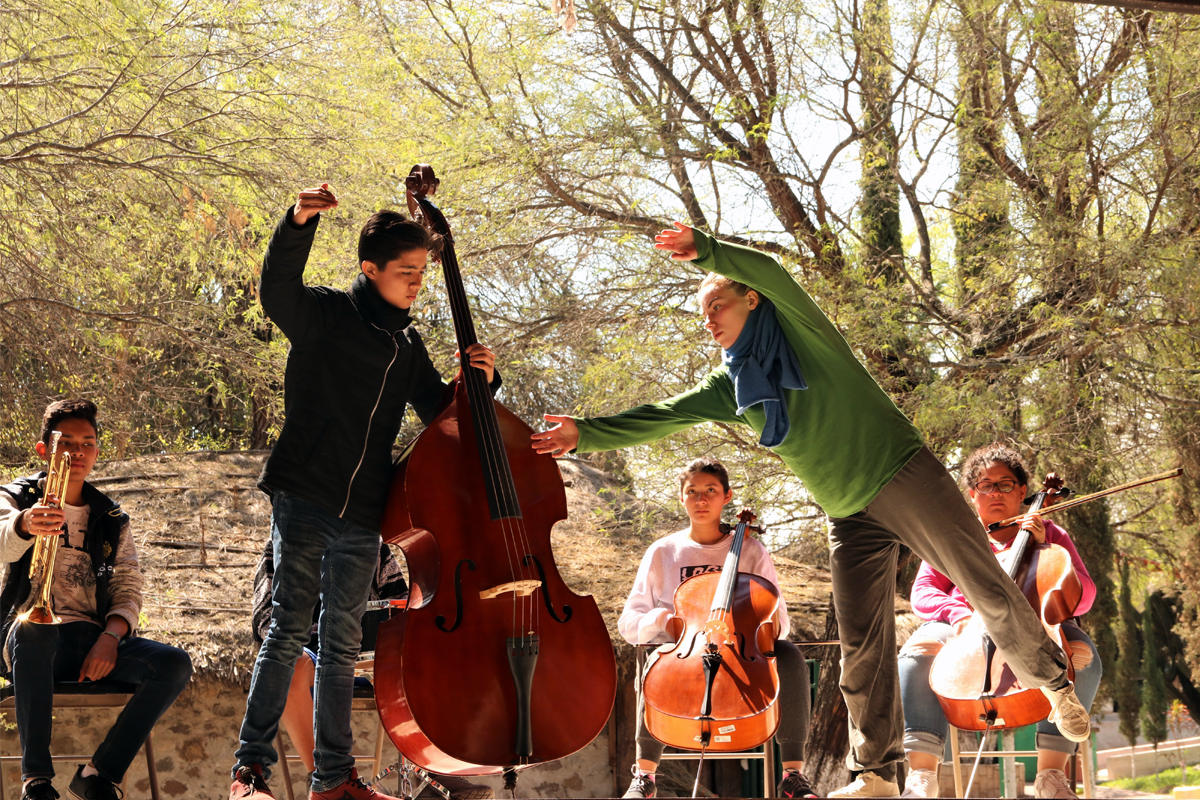 Jugendliche mit klassischen Musikinstrumenten stehen und sitzen vor Bäumen.