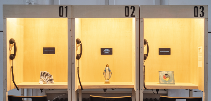In drei offene Telefonkabinen sind jeweils alte 100-D-Mark-Scheine, eine Marienstatue und eine Schalplatte zu sehen. 